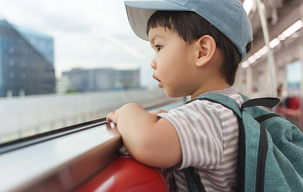 istock Little Asian boy wearing a cap and backpack leaning on the train window, looking outside curiously. 2219513370