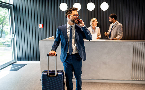 istock Businessman making a phone call while pulling luggage in hotel lobby 2219516584
