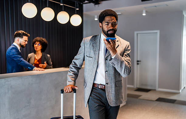 istock Businessman using smartphone while walking in hotel lobby with luggage 2219517257