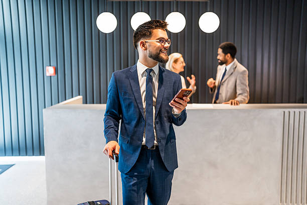 istock Businessman using smartphone while walking in hotel lobby with luggage 2219518719