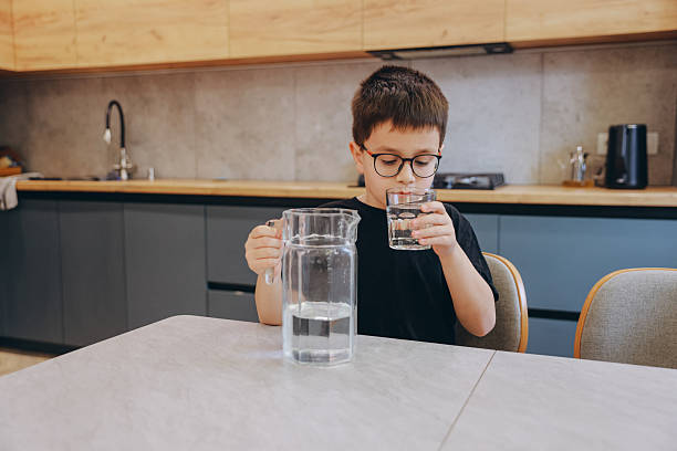 istock Little Boy Pouring Water into Glass in Kitchen 2219519305