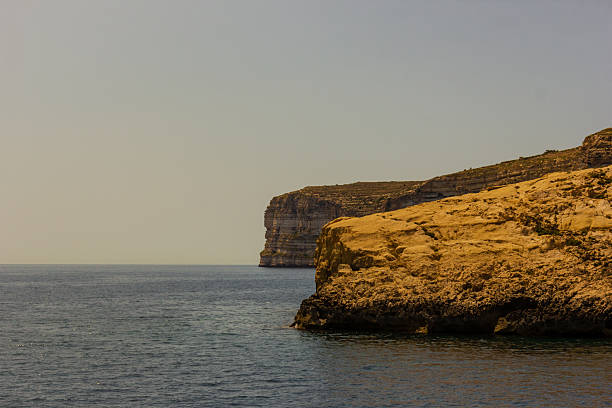 Dramatic rocky coastline with sheer limestone cliffs overlooking calm blue waters under a bright sky, capturing a serene and picturesque seascape ideal for travel, nature, and coastal themes.