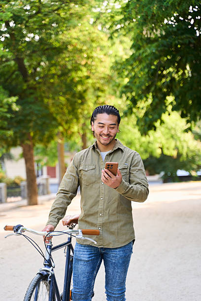 Young man walking with bicycle and using smartphone in park