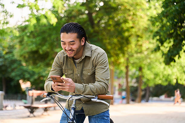 istock Young man smiling and using smartphone while riding bicycle in park 2219529048