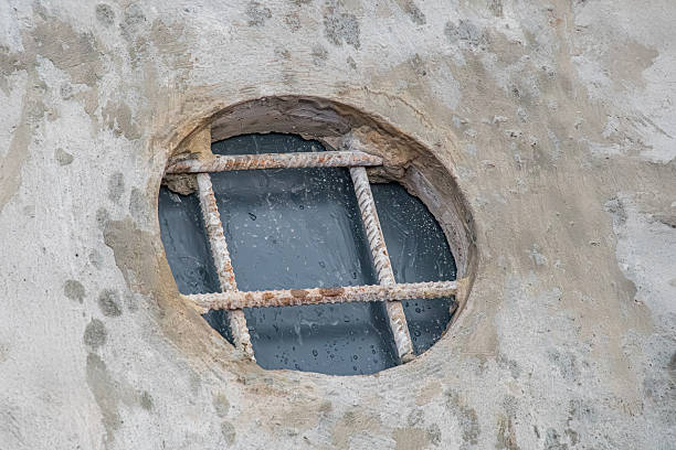 istock Close-up image of an old, weathered round window with vertical bars on a discolored wall Natural lighting, possibly daytime No people or text visible Shallow depth of field 2219532870