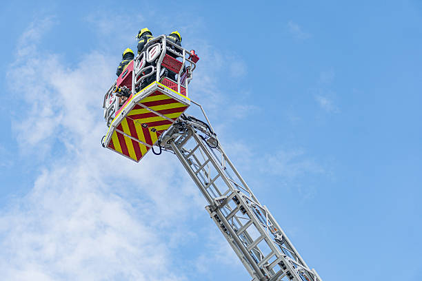 istock Rescue operation underway White fire truck with extended ladder, two firefighters on platform, helmets, red and yellow stripes, high altitude, no text, focus on active scene 2219533564