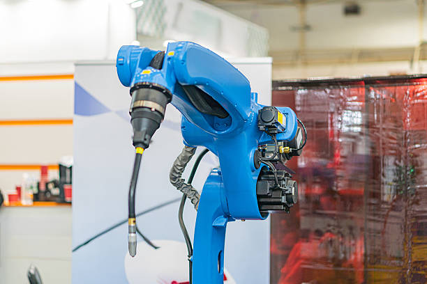 istock An industrial robot, blue with multiple joints and a red-toned adjacent object, is positioned at a workstation in a manufacturing facility The image suggests an assembly line setting with additional 2219533657