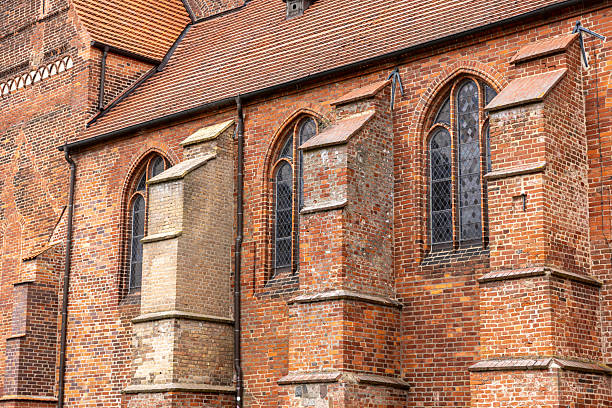 Side view of a historical brick church featuring Gothic arched windows, red masonry buttresses and medieval architecture that evokes spiritual heritage.
