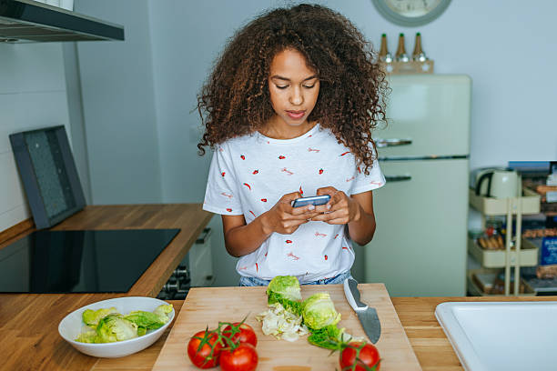 istock Woman in the kitchen with mobile phone, while preparing salad 2219545210