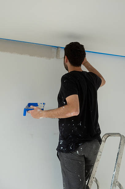 istock Painter using paint roller painting a white wall near the ceiling 2219545274