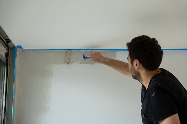 istock Painter using paint roller, painting wall near window, home renovation 2219545346