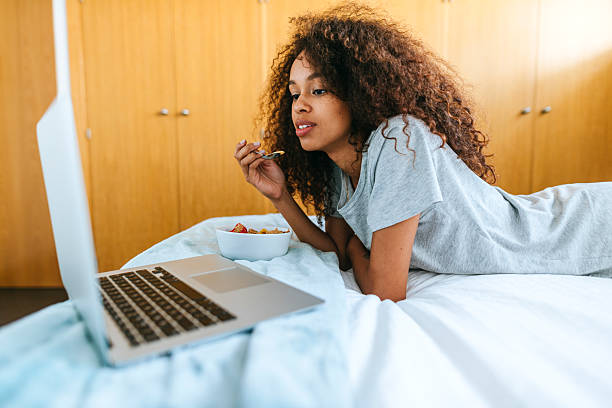istock Woman looking at computer while eating in bed 2219545495