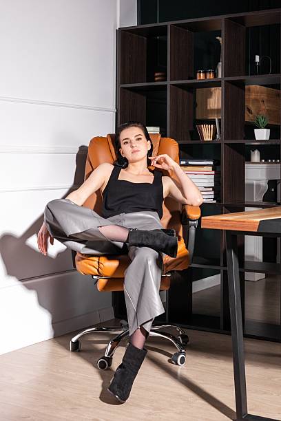 istock Young woman seated in modern office chair striking a confident pose while working on laptop in stylish workspace 2219546153