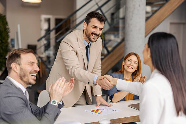 istock Smiling executive shaking hands with successful businesswoman at corporate office while colleagues applauding. 2219547706