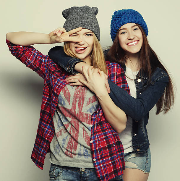 two young girl friends standing together and having fun. Showing signs with hands. Looking at camera