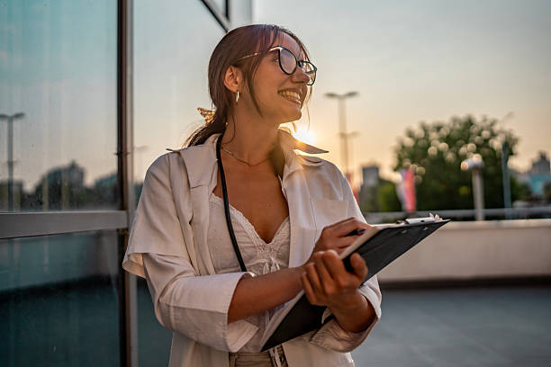 istock Confident Young Professional Woman Smiling Outdoors With Clipboard During Sunset 2219552568