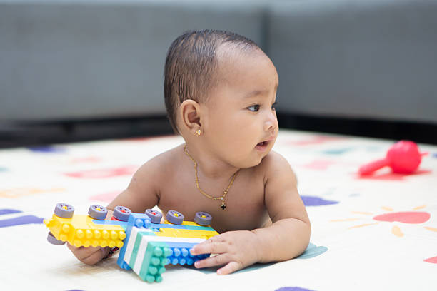A baby lies on the mat while playing independently with colorful building blocks in a home environment.