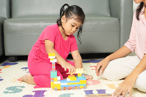A young toddler playing with colorful building blocks alongside an adult in a cozy indoor space.
