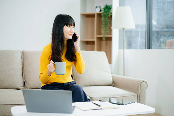 sian woman writing notes while using phone and working remotely with laptop. Ideal for themes of freelance, productivity, multitasking