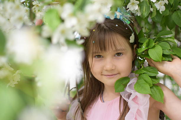 Portrait of a beautiful little girl in the bushes of a blooming apple tree. A doll in his hands.