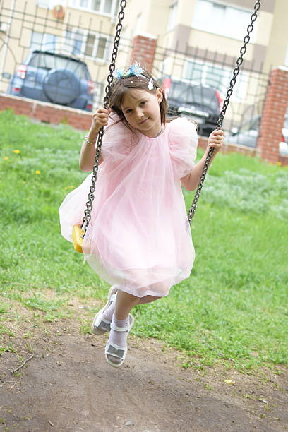 Cute little girl having fun on a playground outdoors on warm summer day. Cute kid swinging outdoors. Summer outdoor leisure for kids.