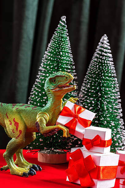 istock Toy dinosaur with gift boxes and mini Christmas trees on red table. Festive and playful holiday scene with a fun prehistoric twist 2219602390