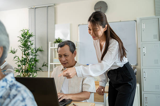 istock Asian female instructor teaching mature students in classroom at school. Attractive teacher motivate and explain senior learner how to use laptop computer during adult education course in tutor class. 2219604647