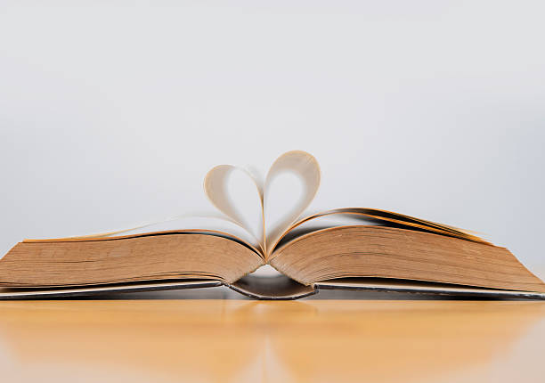 istock Open book with pages shaped like a heart on a wooden table over white background 2219606721
