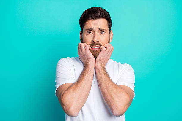 istock Young man expressing nervousness with his hands on face and a turquoise background, conveying anxiety and tension 2219608501