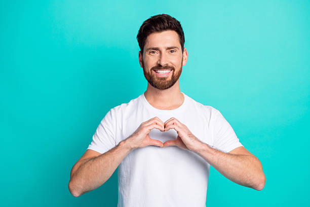 istock Happy young man making a heart gesture with his hands, standing against a teal background, promoting positive emotions 2219608534
