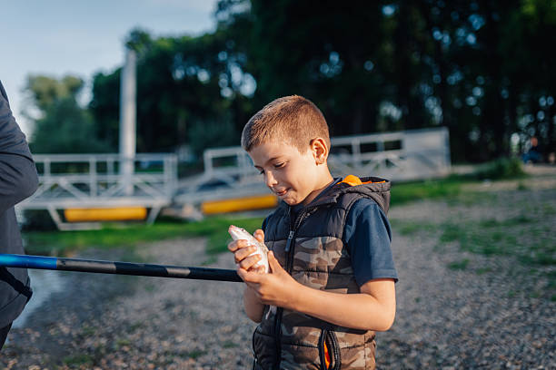Child proudly displaying a small fish caught while fishing with family by a river, enjoying a summer outdoor activity