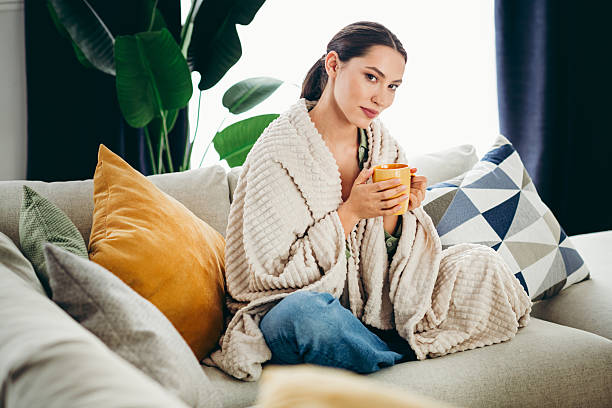 istock Female relaxing in a cozy home setting holding a warm drink while wrapped in a blanket sitting on a sofa on a weekend. 2219610830