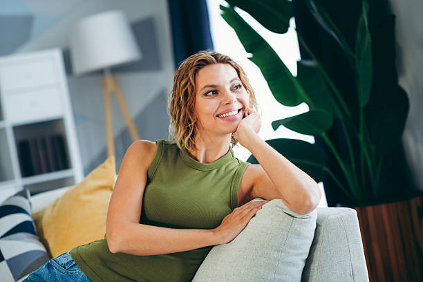 istock Young woman relaxing at home on a cozy couch with cheerful expression surrounded by modern stylish interior and houseplants 2219611099