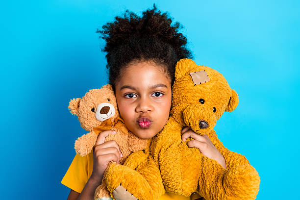 istock Charming young girl hugging teddy bears with playful expression against a vibrant blue background 2219611433