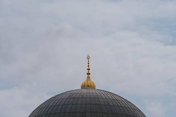 Golden crescent moon rising above mosque dome under cloudy sky