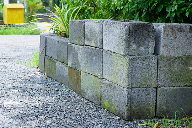 Weathered grey concrete blocks form a low retaining wall in a garden setting providing a rustic and natural aesthetic.