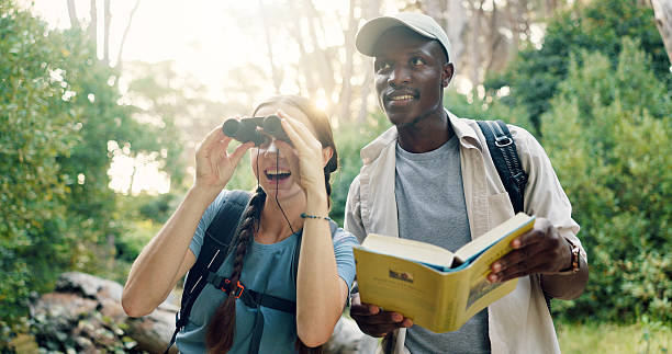 istock Binoculars, travel and couple with birdwatching in forest, book for info and knowledge of species in nature. Surprise, people and view with sightseeing, hiking and trekking with animal text in woods 2219614690