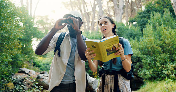 istock Binoculars, travel and people with birdwatching in forest, book for info and knowledge of species in nature. Friends, man and woman with sightseeing, exploring and trekking with animal text in woods 2219614694