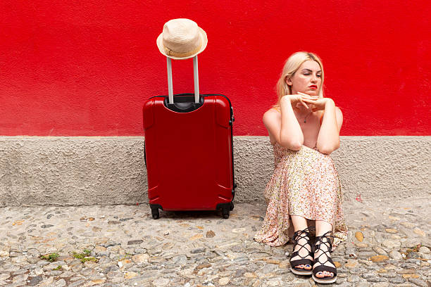 Asian girl in straw hat and yellow dress with big black suitcase among green trees. Summer vacation. Time to travel