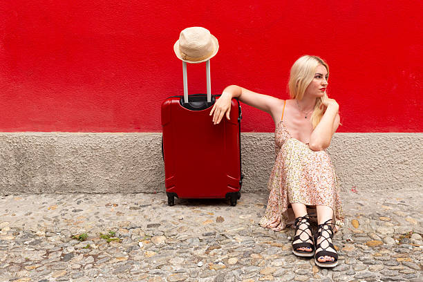 A 2-3 year old sits on a vintage suitcase on a dirt road.