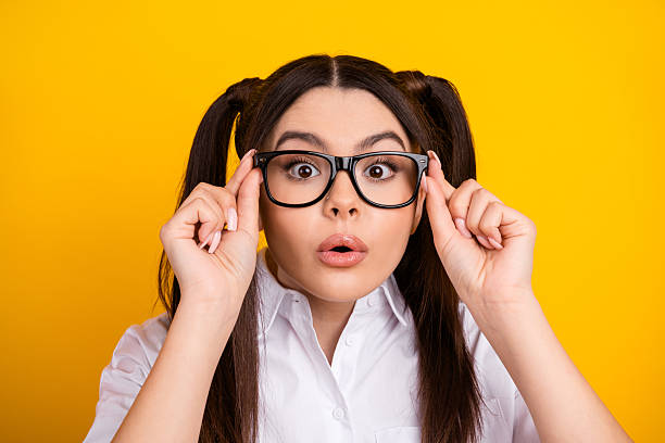 istock Young brunette woman in glasses expressing surprise while holding her frames, standing against a yellow background 2219616330