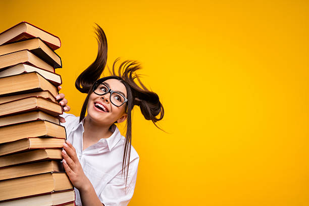 istock Excited student with stacks of book posing against a bright yellow background emphasizing education and joy 2219616422