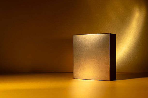 Golden square box standing on a glowing golden surface with dramatic light and shadow