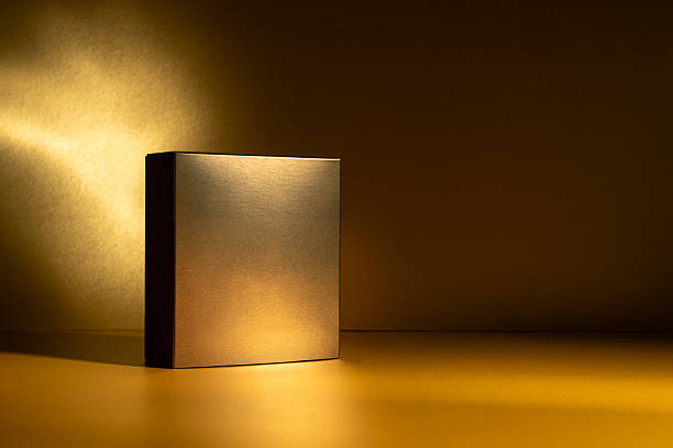 istock Golden square box standing on a glowing golden surface with dramatic light and shadow 2219619624