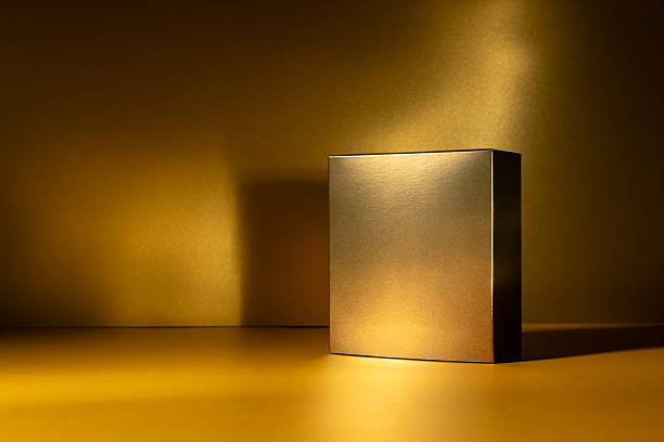 istock Golden square box standing on a glowing golden surface with dramatic light and shadow 2219619625