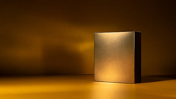istock Golden square box standing on a glowing golden surface with dramatic light and shadow 2219619635