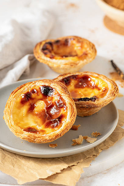 istock Three Pastel de Nata, Portuguese custard tarts, are presented on a plate with cinnamon and vanilla beans. 2219620572