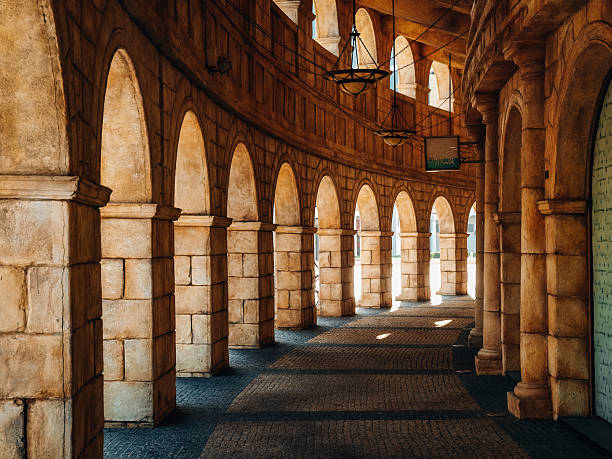Sunlit Stone Archway In Macau: Elegant Curved Colonnade With Repeating Arches And Warm Shadows Evoking Classical Roman Architecture In A Historic-Style Setting. High quality photo