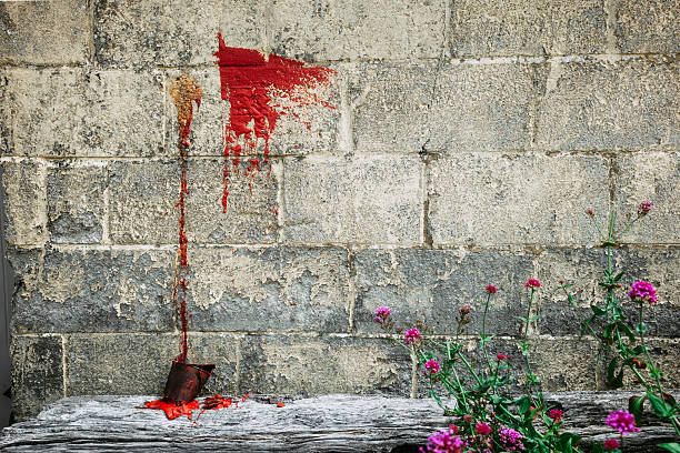 Congealed red paint runs down a breezeblock walll.  The old rusted paint can rests on a piece of wood below.