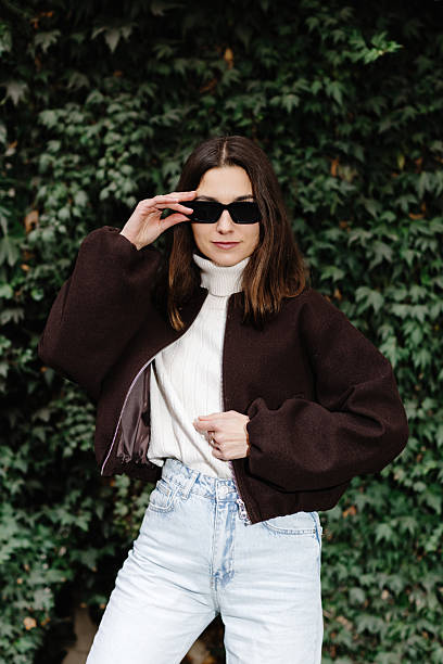 istock Stylish woman adjusting sunglasses while posing near ivy wall 2219623989